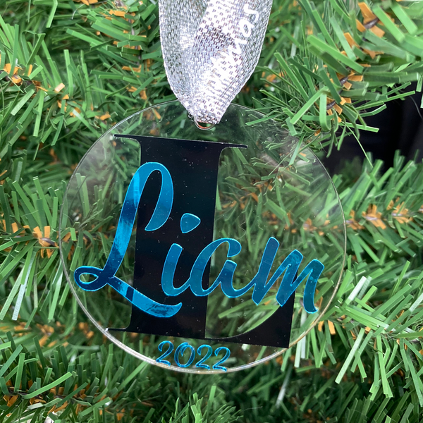 Gepersonaliseerd kerstornament. Gemaakt van een 7cm schijf van acryl. Hierop wordt met zwart vinyl de eerste letter van de naam bedrukt. De naam en het geboorte jaar worden in een kleur vinyl naar keuze gemaakt. Een leuk kerstcadeau.