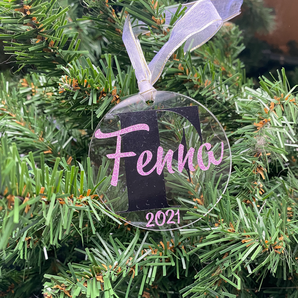 Gepersonaliseerd kerstornament. Gemaakt van een 7cm schijf van acryl. Hierop wordt met zwart vinyl de eerste letter van de naam bedrukt. De naam en het geboorte jaar worden in een kleur vinyl naar keuze gemaakt. Een leuk kerstcadeau.