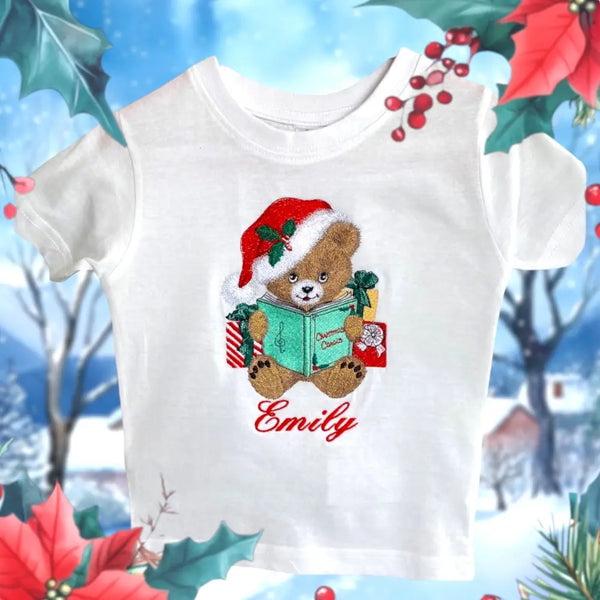 Kerstshirt voor kinderen met geborduurde kerstbeer in kerstmuts en naam, omringd door kerstcadeaus en een boek met Christmas Carols.