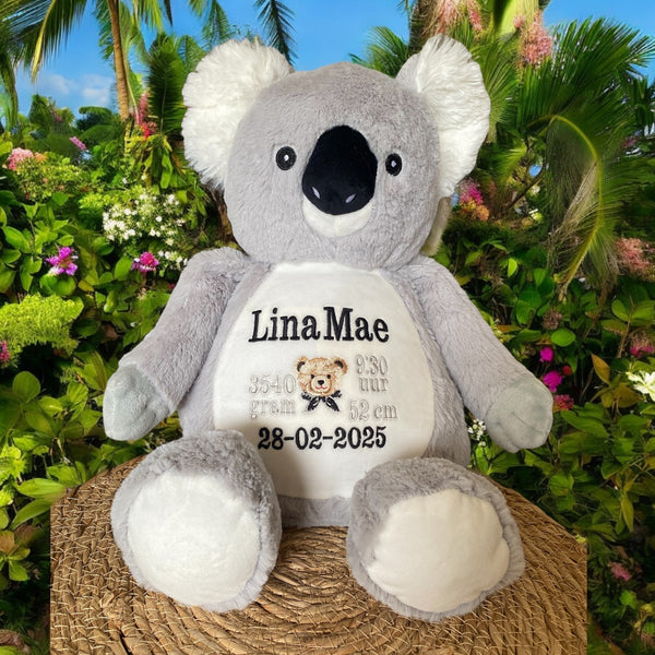 Grijze geboorteknuffel in de vorm van een koala met gepersonaliseerd borduurwerk op de buik, inclusief naam en geboortegegevens.