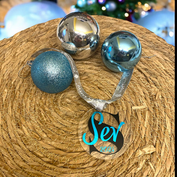 Gepersonaliseerd kerstornament. Gemaakt van een 7cm schijf van acryl. Hierop wordt met zwart vinyl de eerste letter van de naam bedrukt. De naam en het geboorte jaar worden in een kleur vinyl naar keuze gemaakt. Een leuk kerstcadeau.