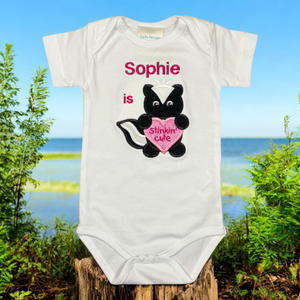 Een gepersonaliseerd baby rompertje met geborduurd Stinkdiertje die een roze hart met de tekst stinking cute vasthoudt. De rompertjes zijn beschikbaar in wit en zwart. In combinatie met kraamcadeau set Ivoor uniek als kraamcadeautje.