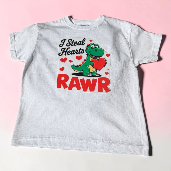 Leuk kindershirt met groene dinosaurus die een rood hart vasthoudt en de tekst "I Steal Hearts RAWR".