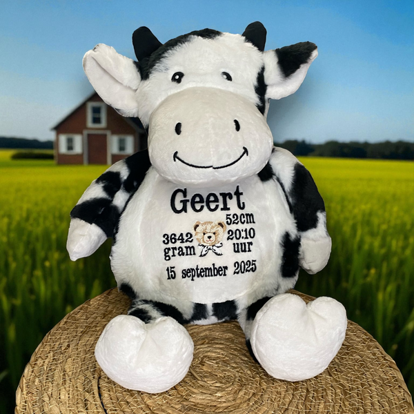 Zwart-witte geboorteknuffel in de vorm van een koe, zittend met geborduurde geboortedetails op de buik zoals naam, datum en gewicht – uniek kraamcadeau.