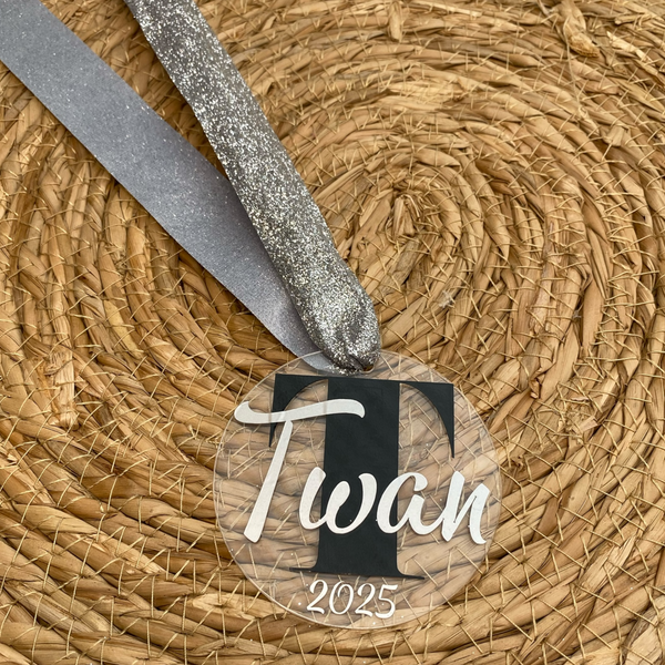 Gepersonaliseerd kerstornament. Gemaakt van een 7cm schijf van acryl. Hierop wordt met zwart vinyl de eerste letter van de naam bedrukt. De naam en het geboorte jaar worden in een kleur vinyl naar keuze gemaakt. Een leuk kerstcadeau.