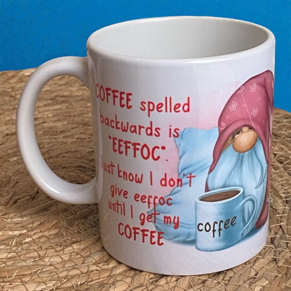 Op de afbeelding: Een witte keramische koffiemok met een rode en witte gnome-illustratie. De mok heeft de tekst "COFFEE spelled backwards is 'EEFFOC'. Just know I don't give eeffoc until I get my COFFEE" erop gedrukt.