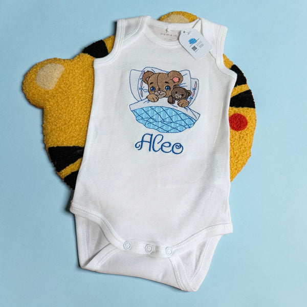 Geborduurd en gepersonaliseerd baby rompertje met een beertje die in bed ligt en een teddy beer vasthoudt. Onder het in bed liggende beertje wordt in het blauw de naam van de baby geborduurd. Echt een super leuk geboorte cadeau.