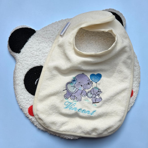 Een handgemaakt slabbetje met 2 geborduurde olifanten. Het baby olifantje schommelt en houd een ballon hart vast. Door onder de olifanten de naam van de baby te laten borduren heeft u een origineel en uniek gepersonaliseerd kraamcadeau.