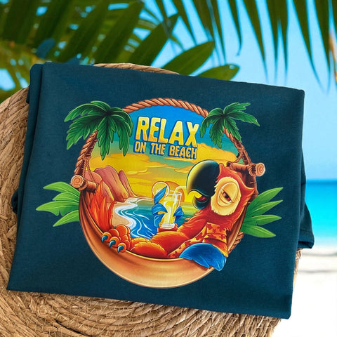 T-shirt met kleurrijk tropisch design van een relaxte papegaai in hangmat, omringd door palmbomen en zonsondergang met tekst “RELAX ON THE BEACH” – unisex zomershirt van Sazudesigns.