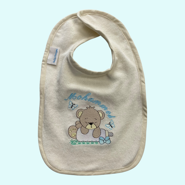 Handgemaakt slabbetje met geborduurde beer hangend over een baby melkfles. Het slabbetje wordt gepersonaliseerd met de naam van de baby. Een uniek kraamcadeau die niet in de winkel verkrijgbaar is.