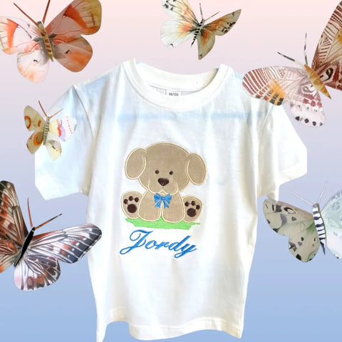 Gepersonaliseerd kinder shirt met een geborduurde applicatie van een beige hondje van Nicky Velours met een blauwe strik. Het hondje voelt zacht aan. Een lief, leuk, zacht kindershirt als cadeau voor de oudere broer.