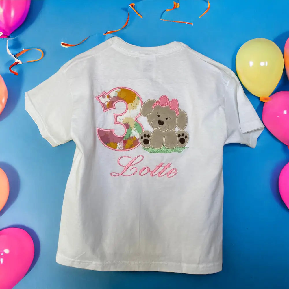 Gepersonaliseerd kindershirt voor een verjaardag. Op het shirt wordt het nummer van de leeftijd geborduurd, met daarnaast een lief beige hondje van zacht  Nickey velours.  Hieronder wordt de naam van de jarige in het roze geborduurd.