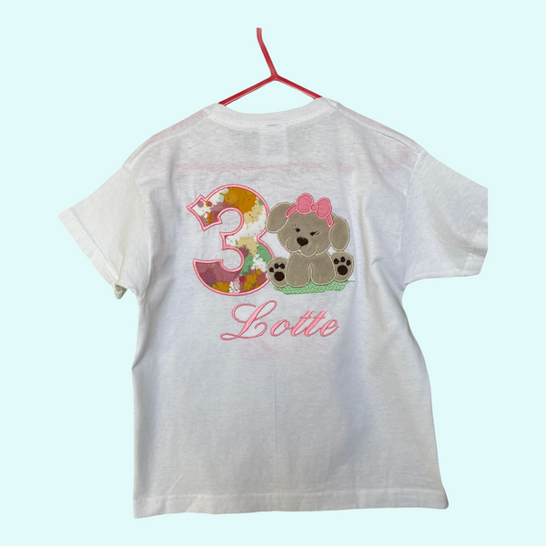 Gepersonaliseerd kindershirt voor een verjaardag. Op het shirt wordt het nummer van de leeftijd geborduurd, met daarnaast een lief beige hondje van zacht  Nickey velours.  Hieronder wordt de naam van de jarige in het roze geborduurd.