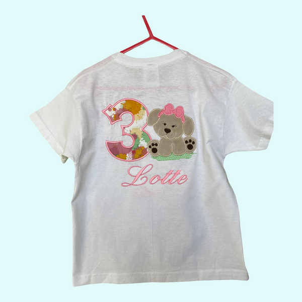 Gepersonaliseerd kindershirt voor een verjaardag. Op het shirt wordt het nummer van de leeftijd geborduurd, met daarnaast een lief beige hondje van zacht  Nickey velours.  Hieronder wordt de naam van de jarige in het roze geborduurd.
